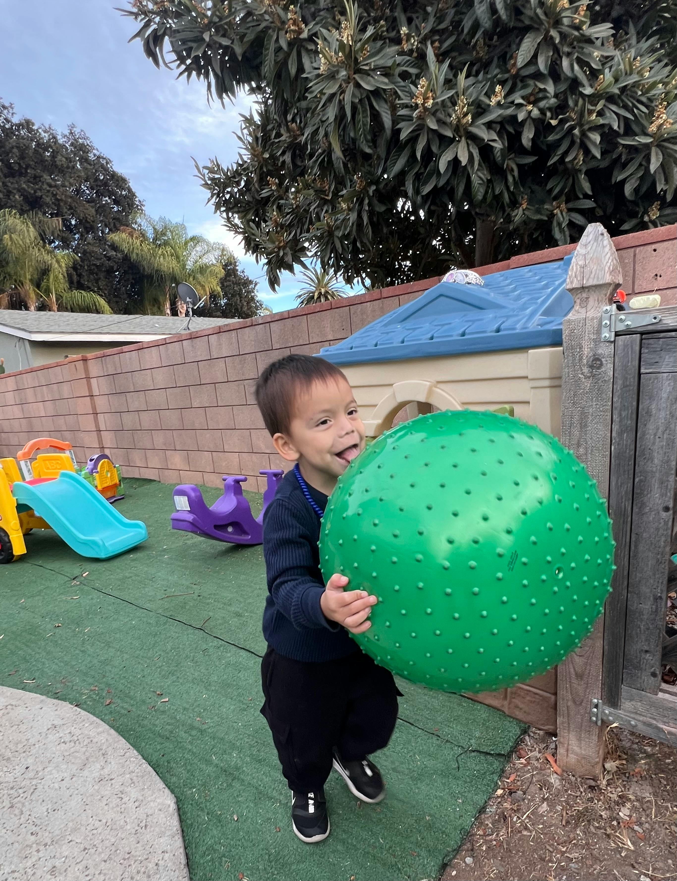 Child holding a large green ball on a playground