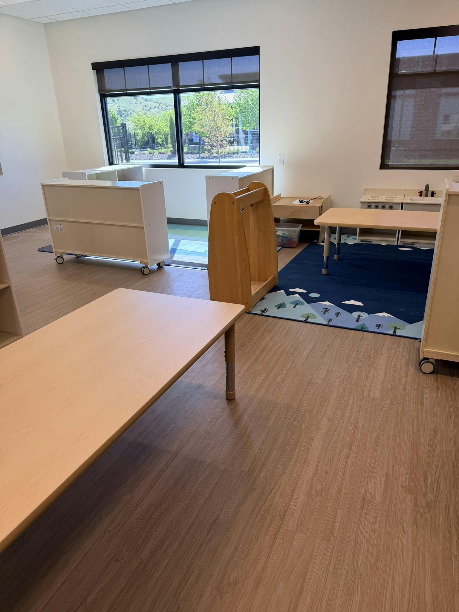 Empty classroom with tables, toy kitchen, and a rug with a mountain design