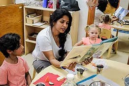 Adult reading a book to two children at a table