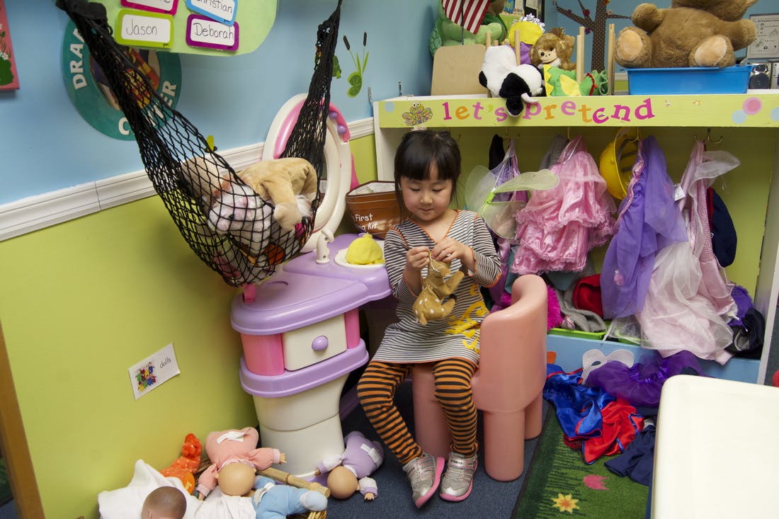 Child sitting at a small table holding a toy in a classroom