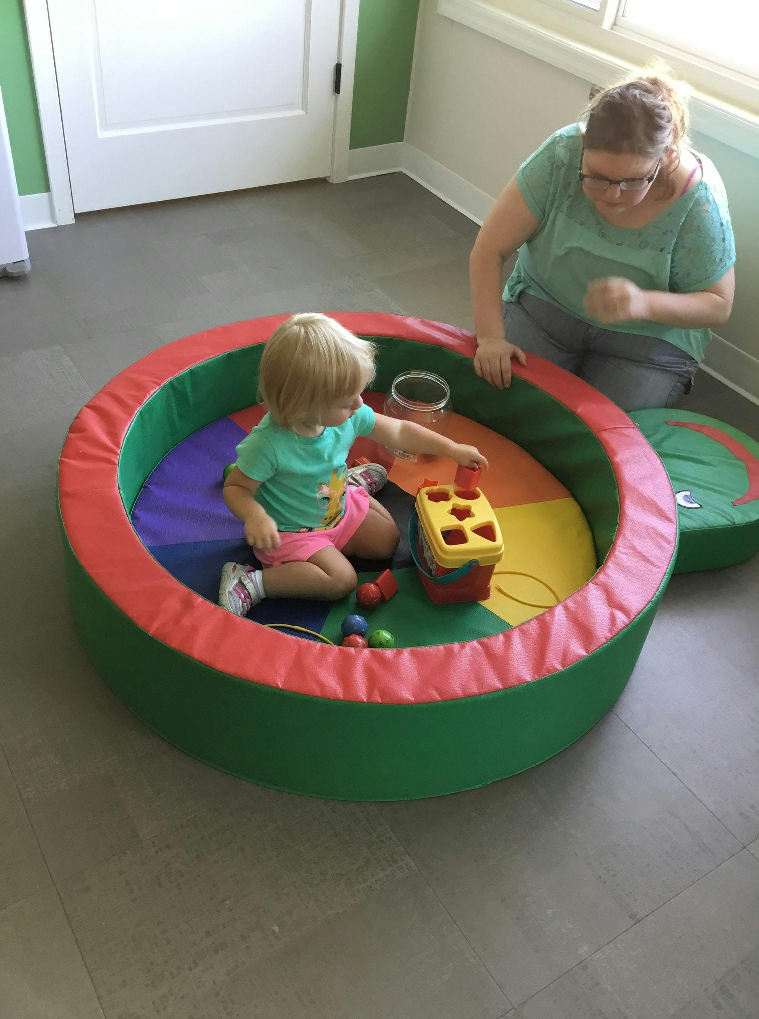 Child playing with a shape sorter in a soft play area with an adult nearby