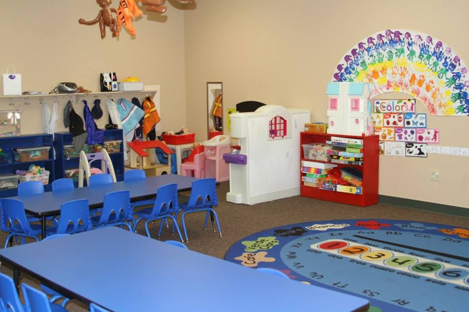 Classroom with blue tables and chairs, and a colorful rug
