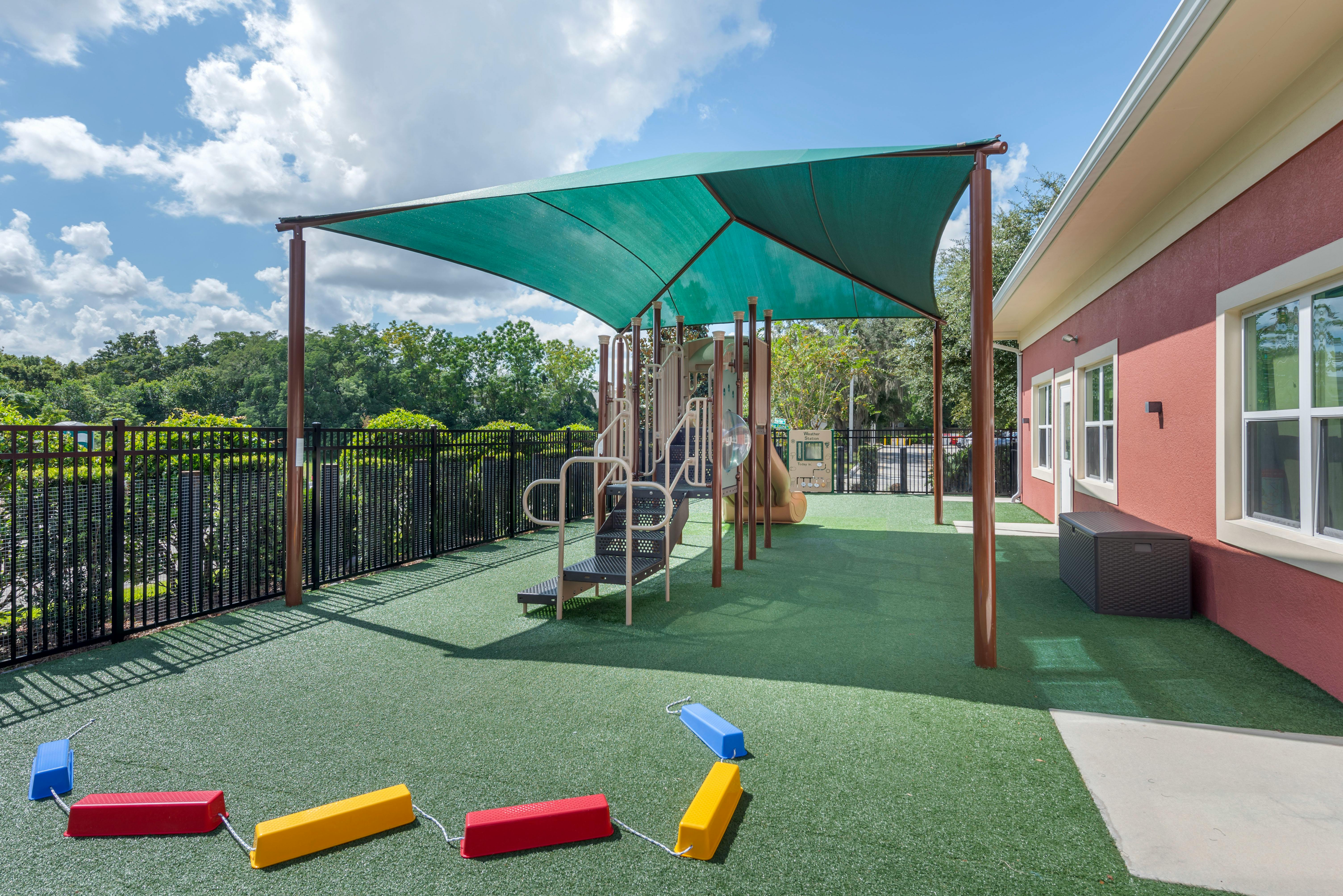 Outdoor playground with green turf, shade canopy, and building