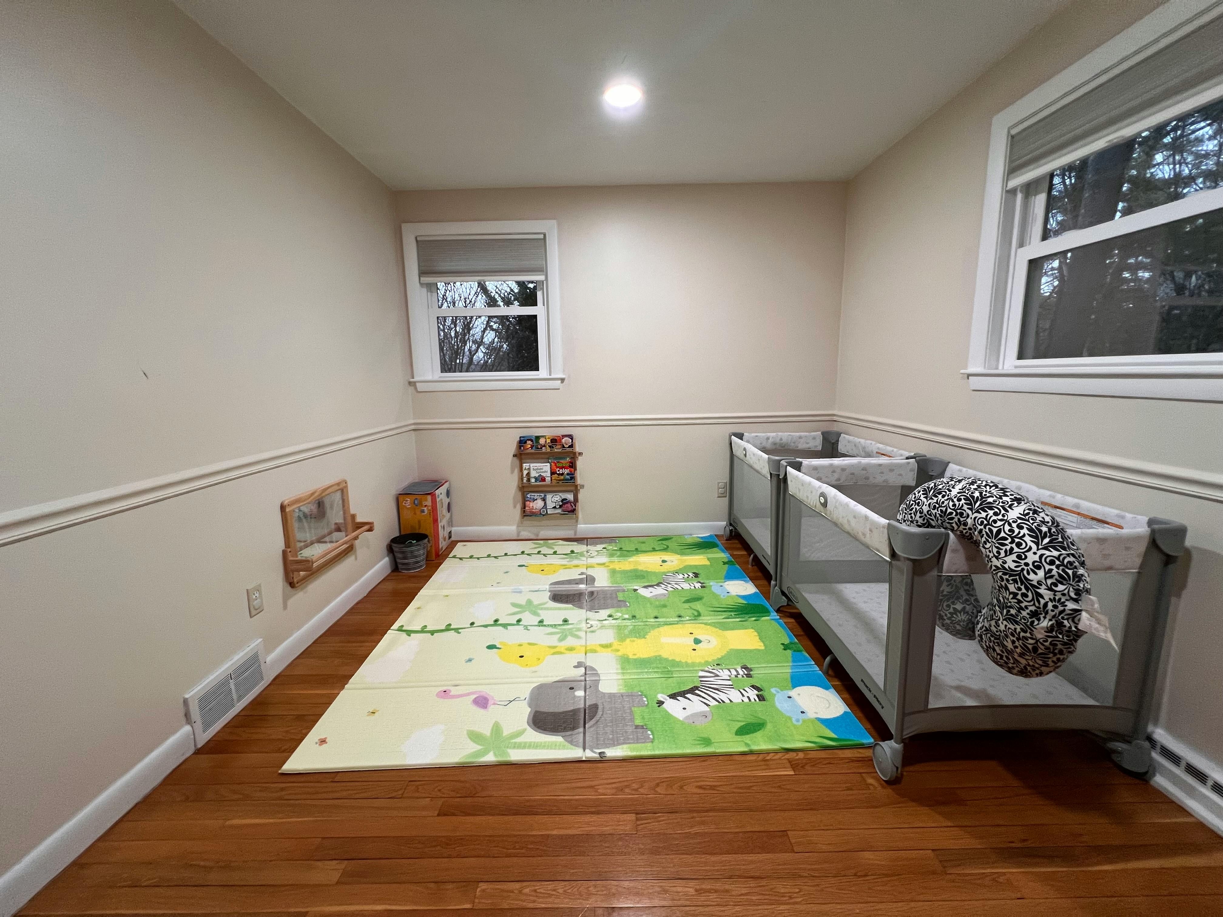 Two cribs in a room with a colorful playmat on the floor