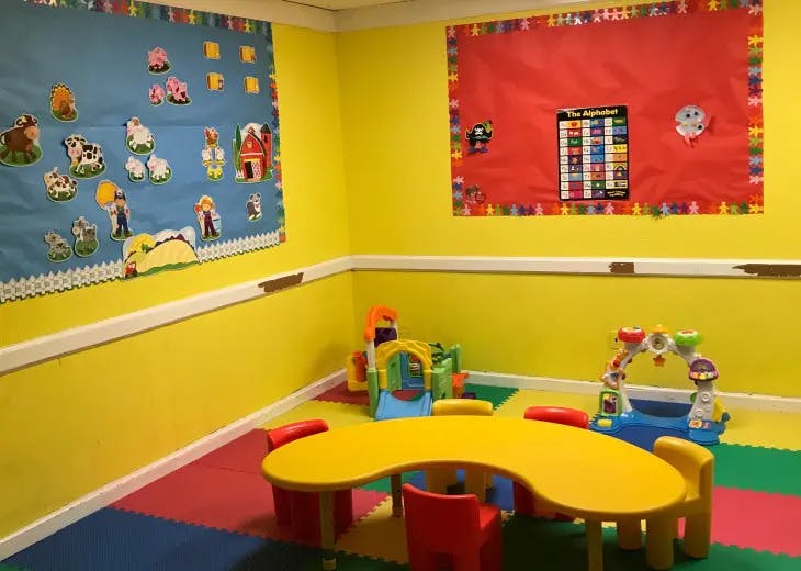 Playroom with yellow table and chairs, colorful floor mats, and bulletin boards