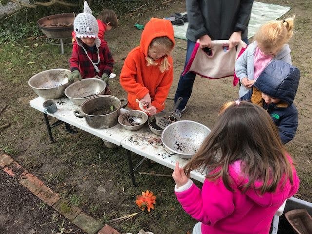 Children playing with bowls and dirt on a table outdoors