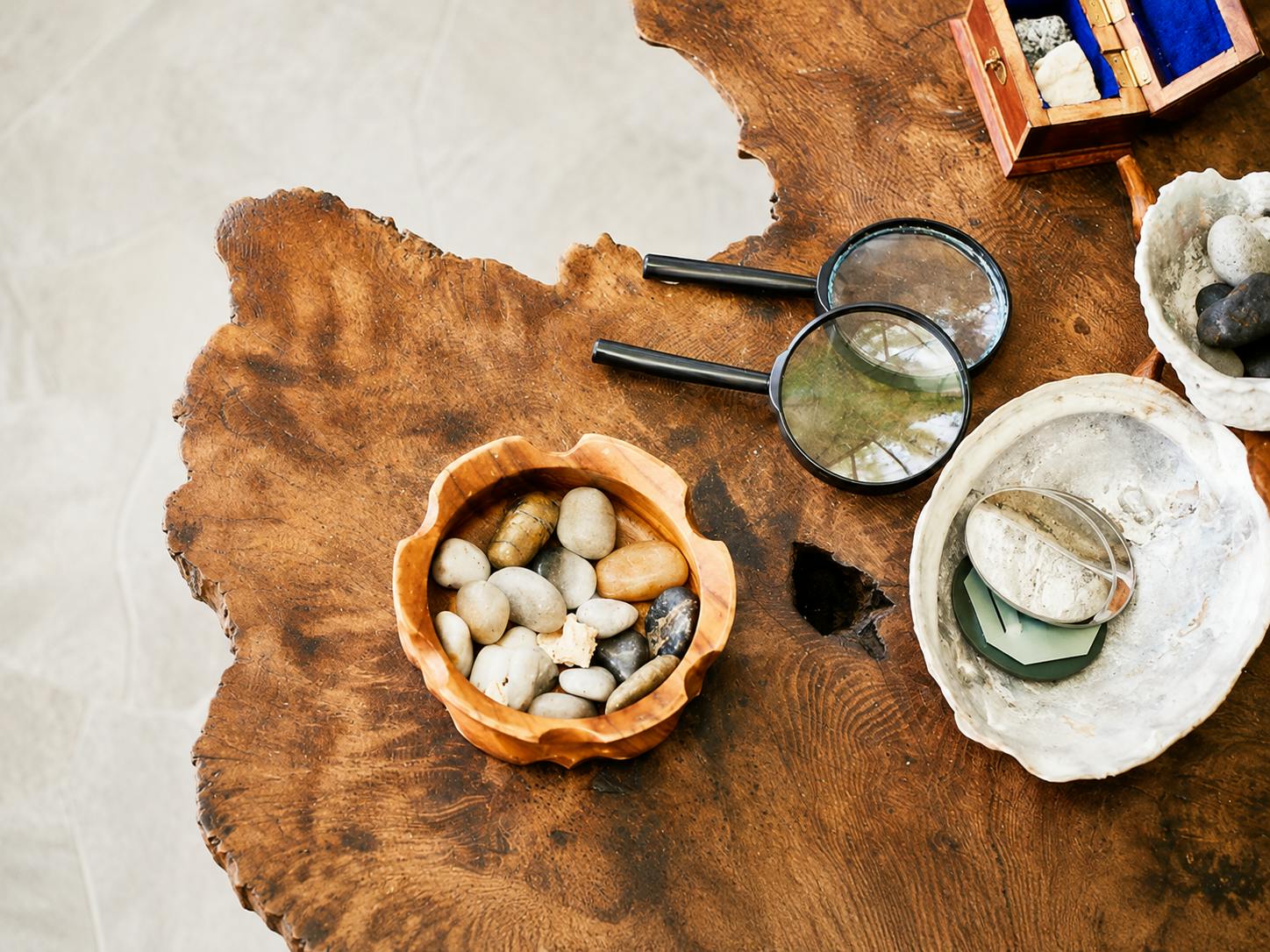 Wooden bowl filled with smooth stones and magnifying glasses on a wooden table