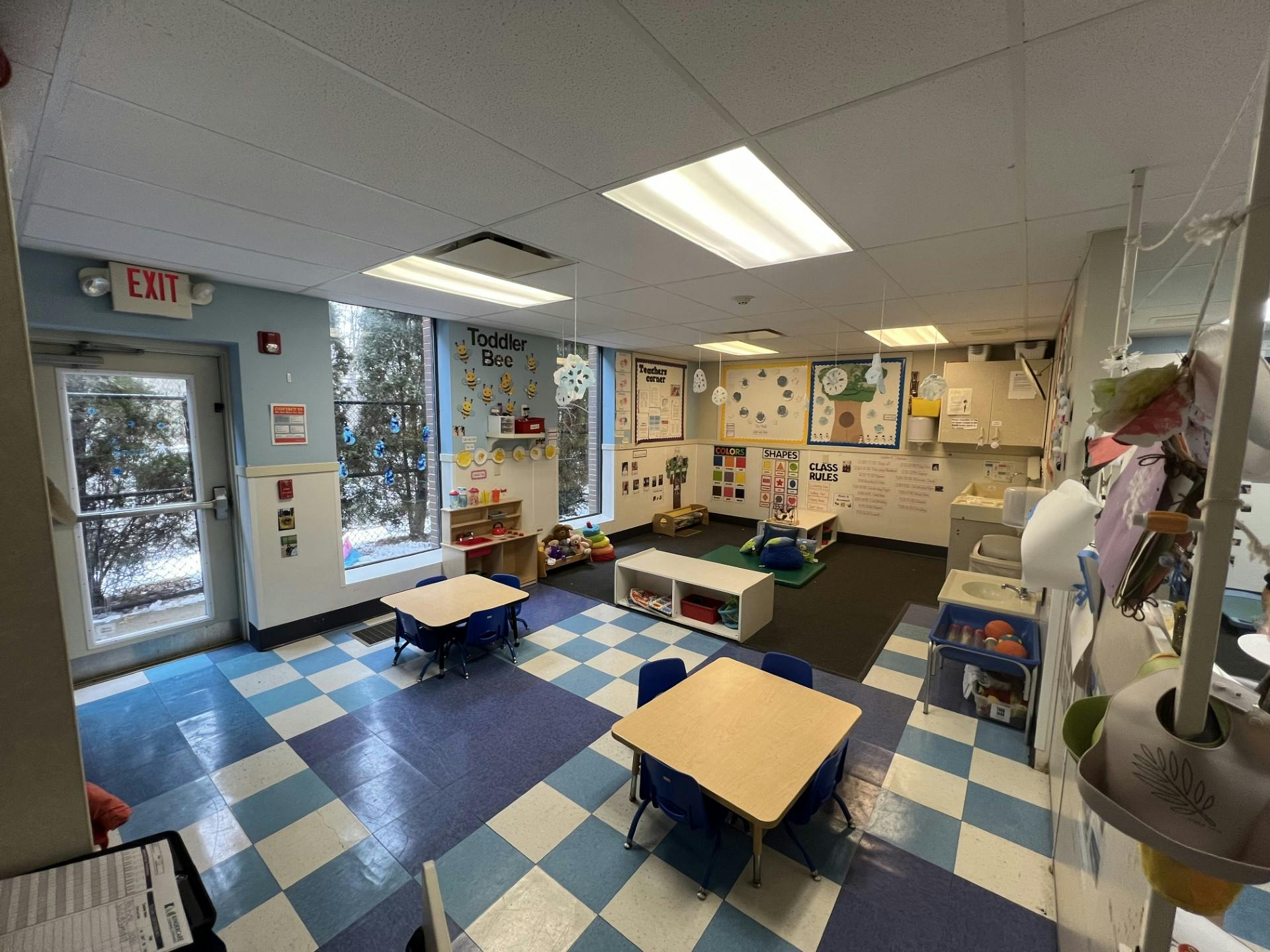A colorful classroom with small tables and chairs, toys, and educational posters