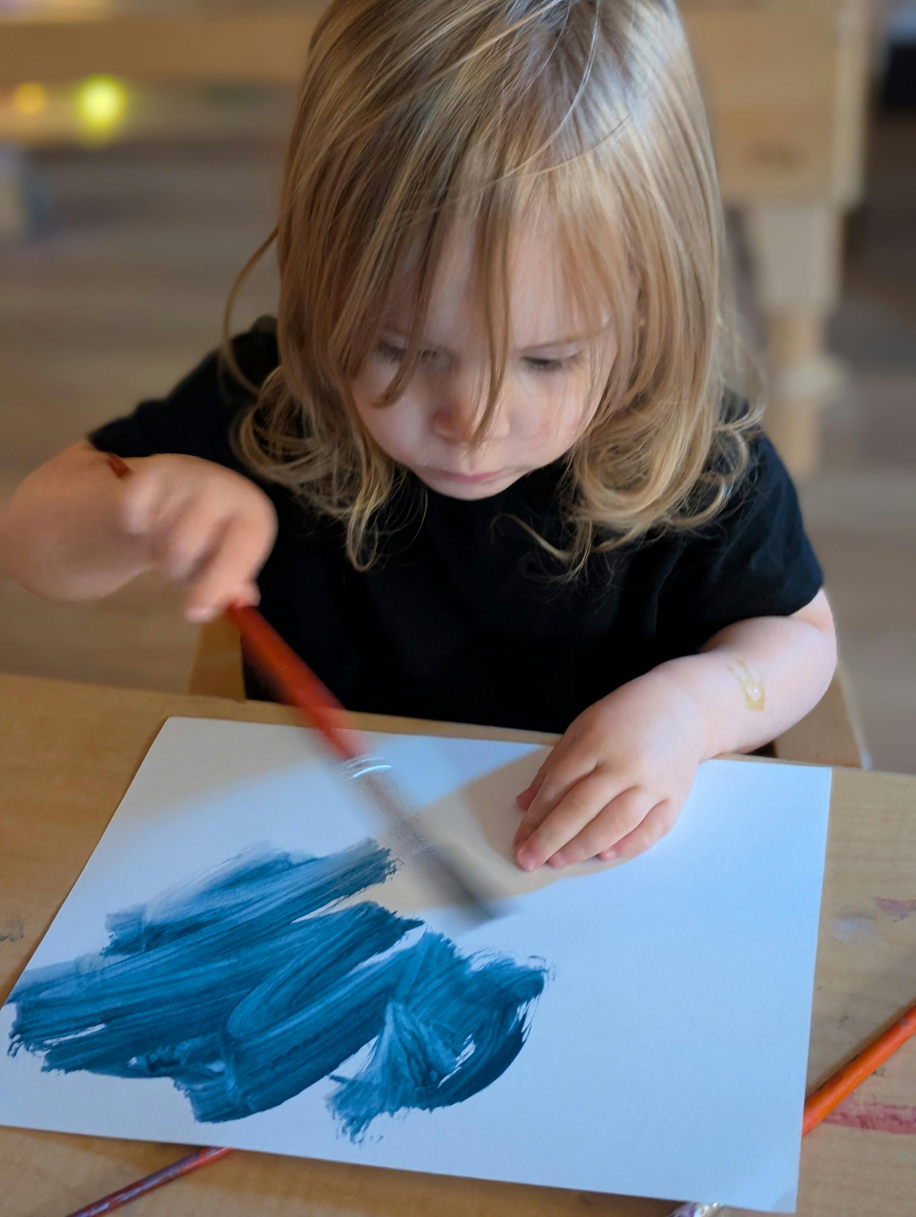Child painting blue strokes on paper with a brush