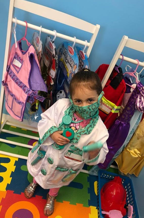Child in a doctor costume and face mask holding a toy stethoscope