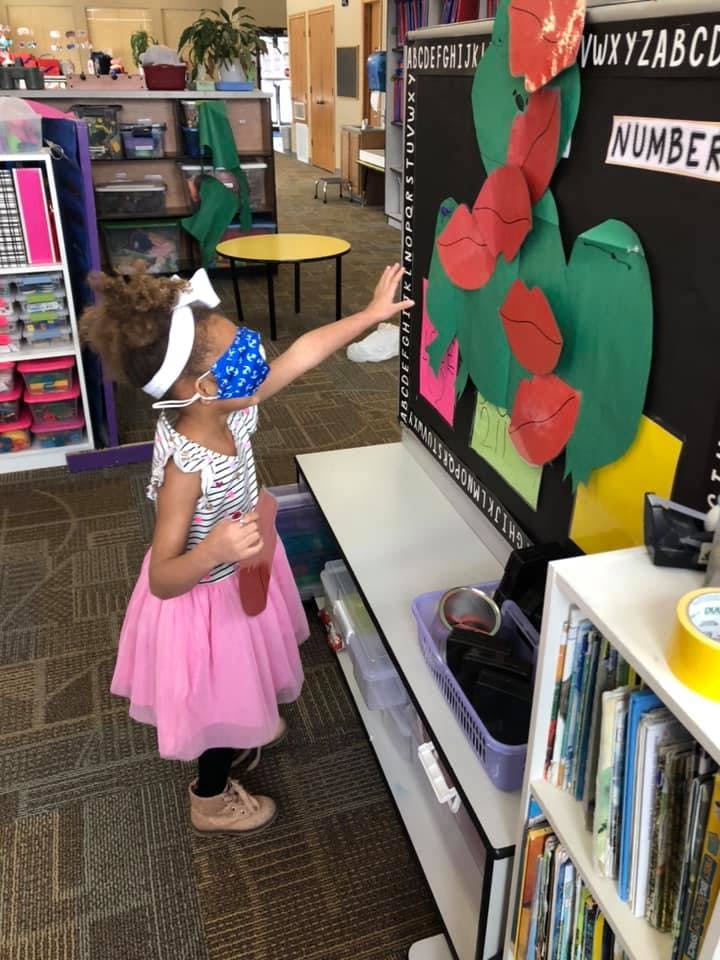 Child in a mask reaching out to a classroom display with a bulletin board
