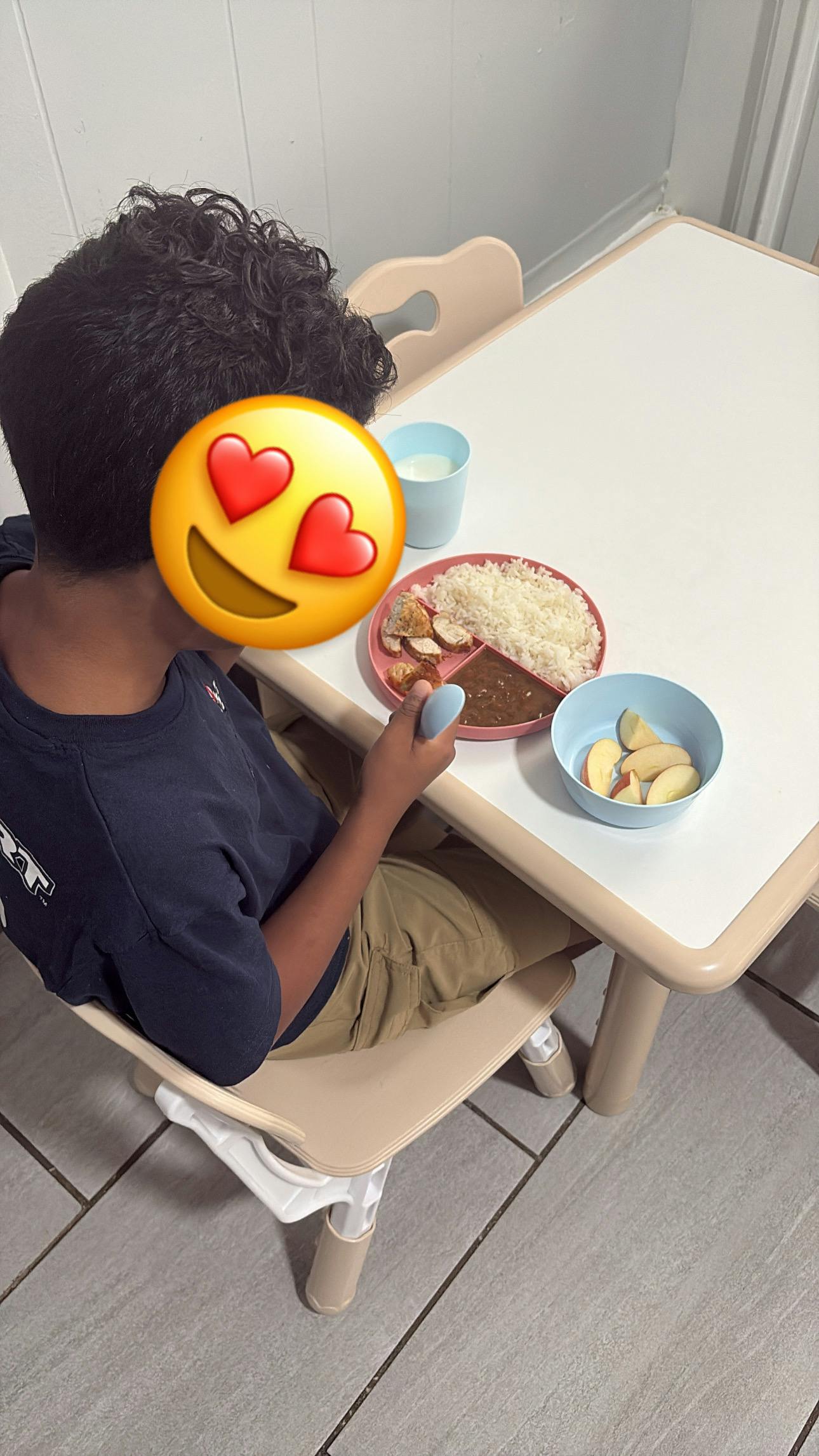 Child sitting at a small table eating a meal of rice and fruit