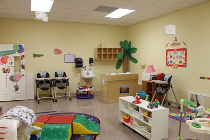 Empty daycare room with high chairs, changing table, and play mats