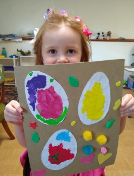 Child holding up a craft project with colorful egg shapes