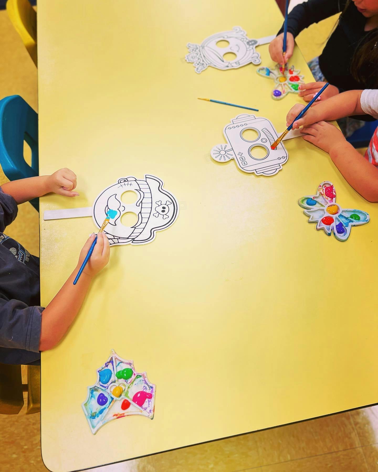 Children painting paper masks and shapes at a table