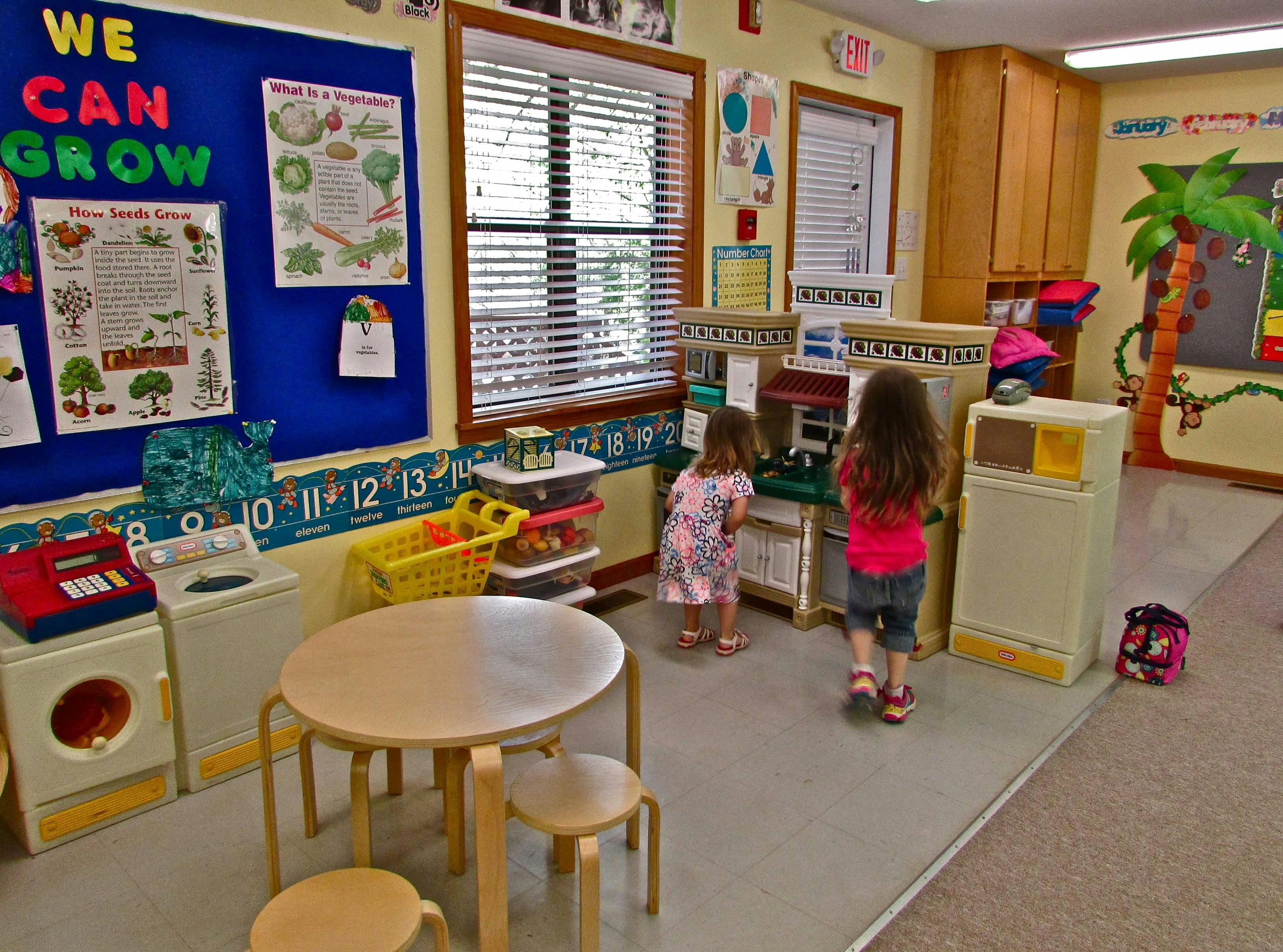 Two children playing in a classroom with toy kitchen appliances
