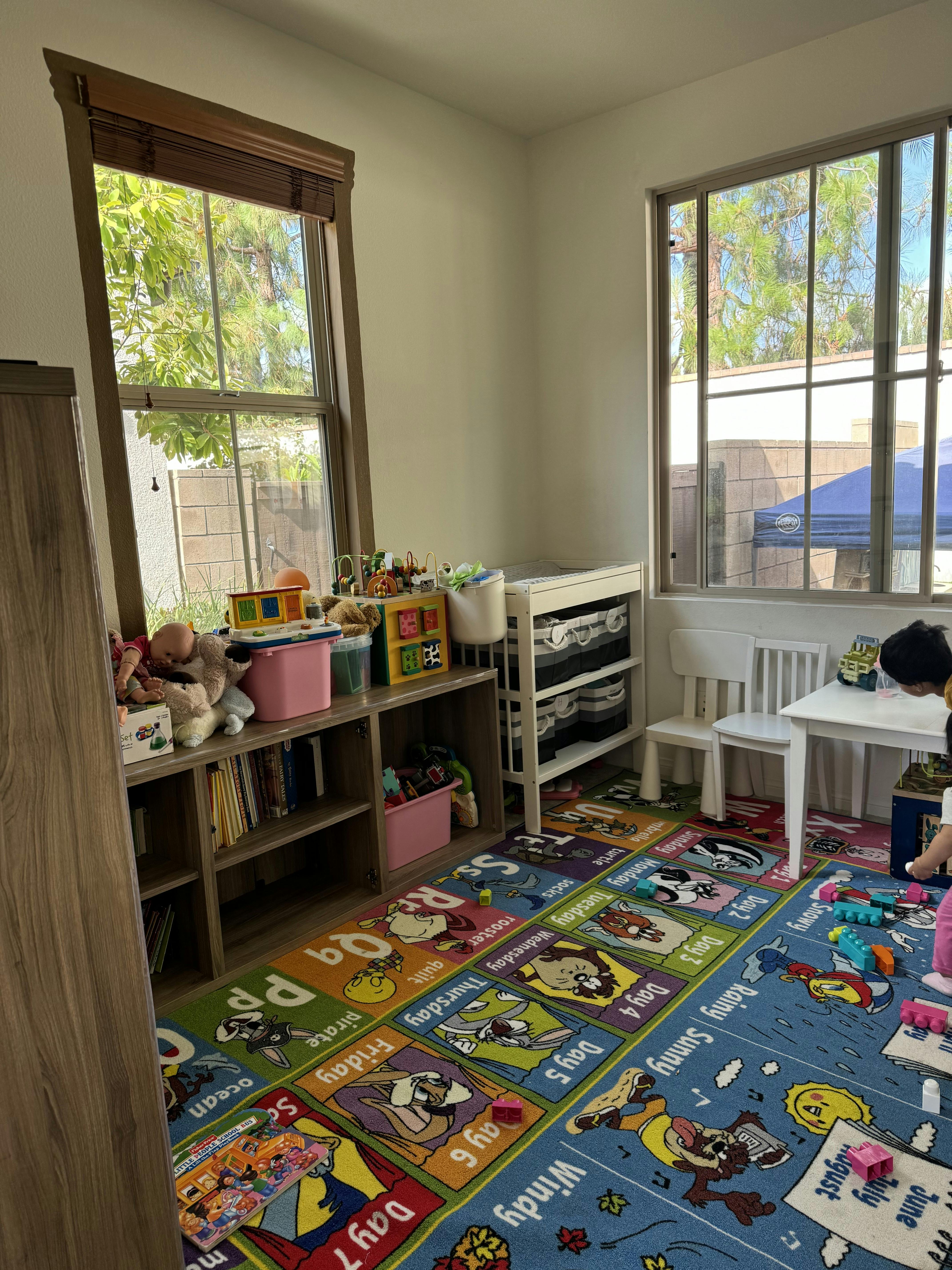child playing on a colorful rug in a playroom filled with toys and windows