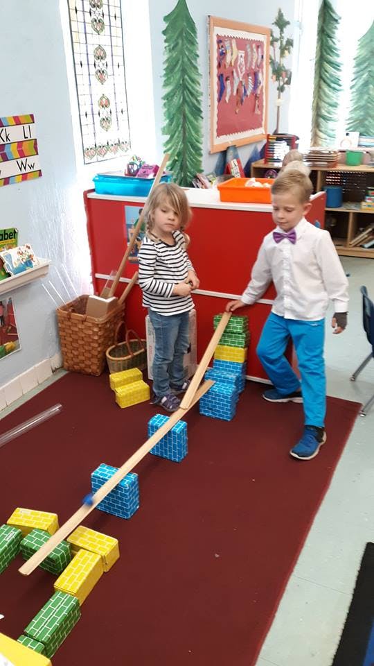 Two children playing with blocks and wooden planks in a classroom