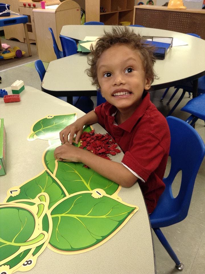 Child at a table with leaf cutouts and red pom-poms