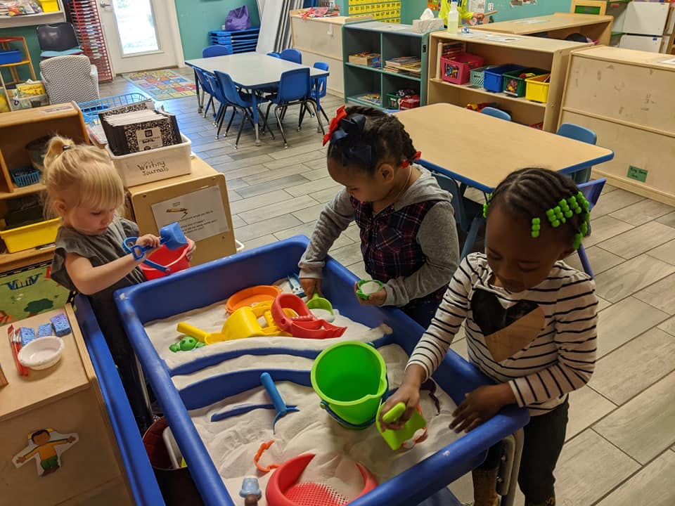 Three children playing in a sand table in a classroom
