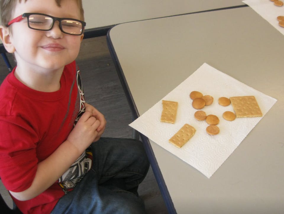 Child in glasses sitting at a table with crackers on a napkin