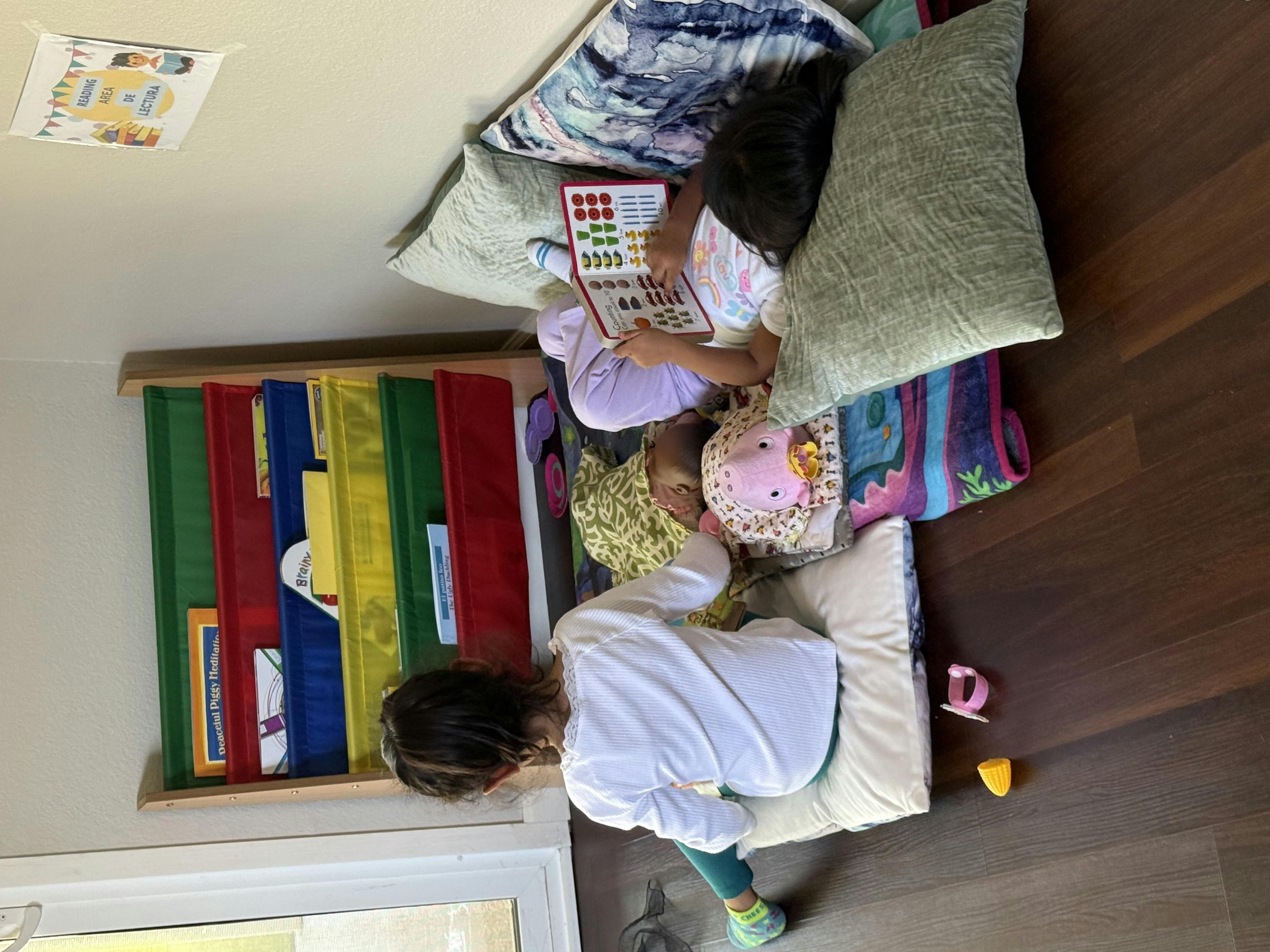 Two children on floor cushions, one reading a book, the other looking at a bookshelf