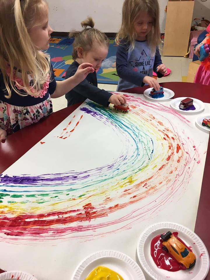 Children making rainbow art with toy cars and paint