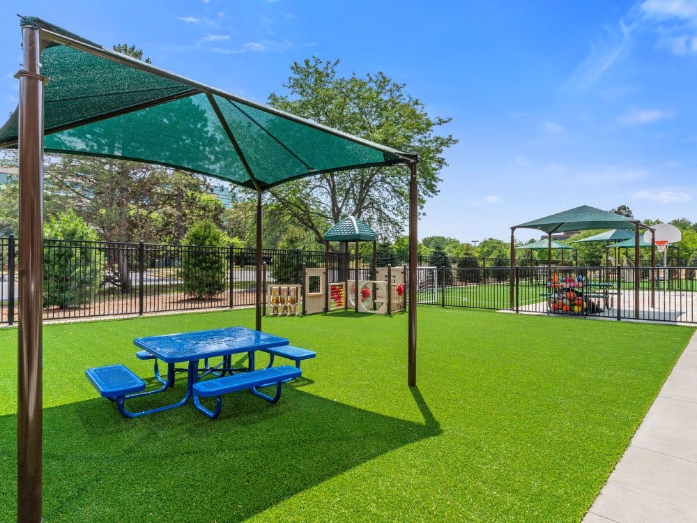 Outdoor playground with artificial turf, blue picnic table, and shade canopy shade canopy