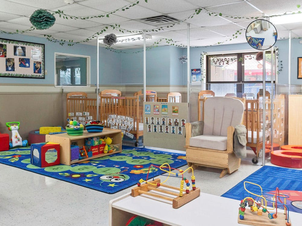 A colorful classroom with cribs, play mats, toys, and a rocking chair