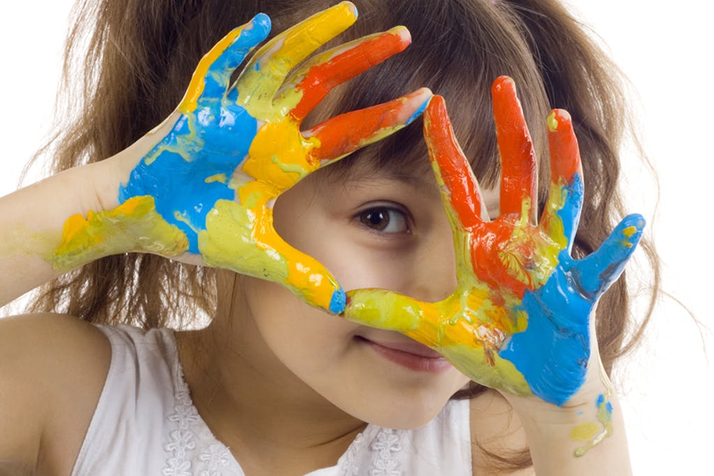 Child with hands covered in paint held up to face