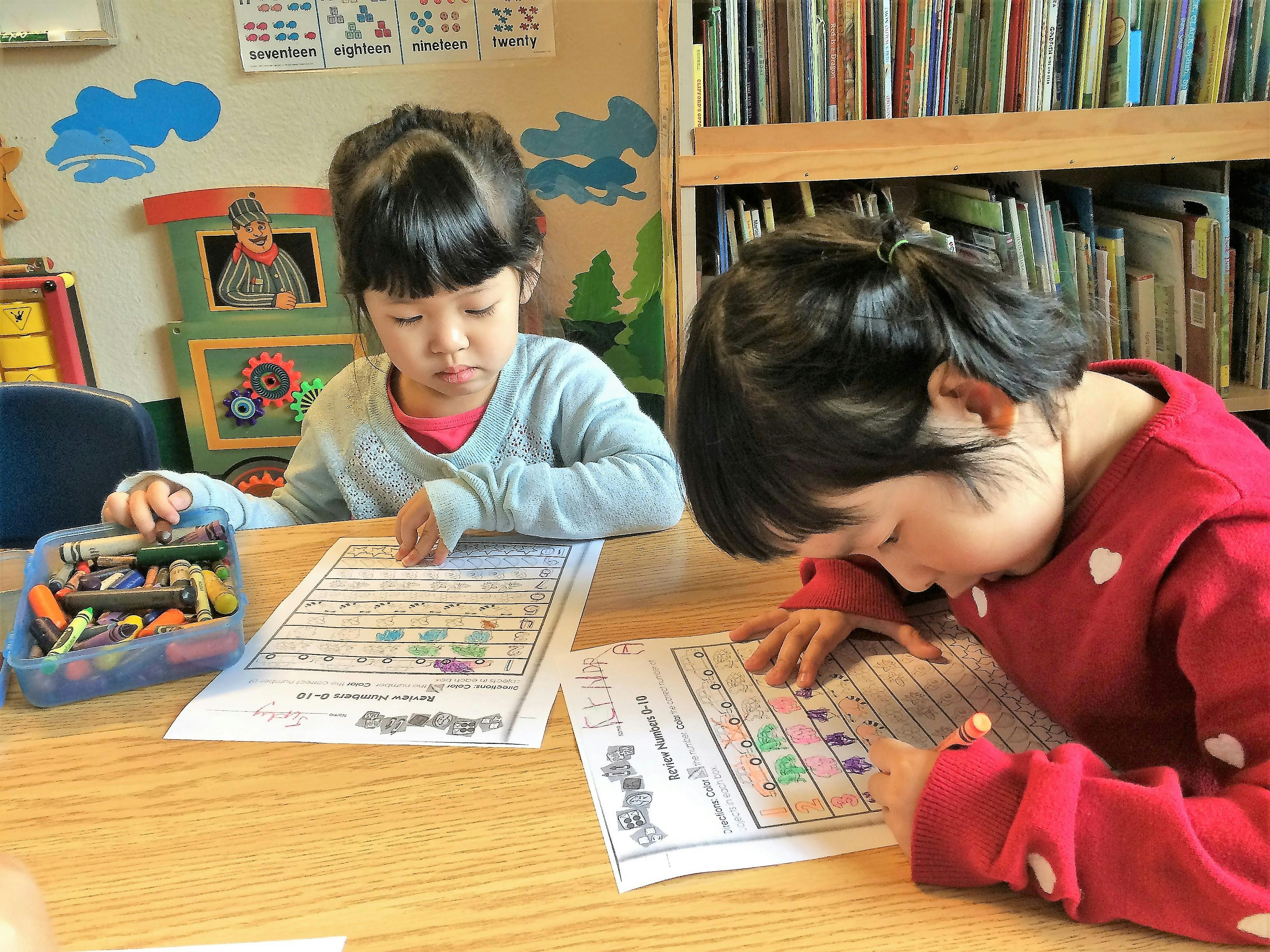 Two children working on papers at a table in a classroom