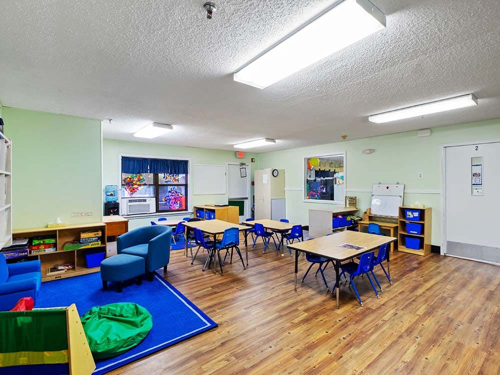 Classroom with blue chairs, small tables, and a blue rug with an armchair