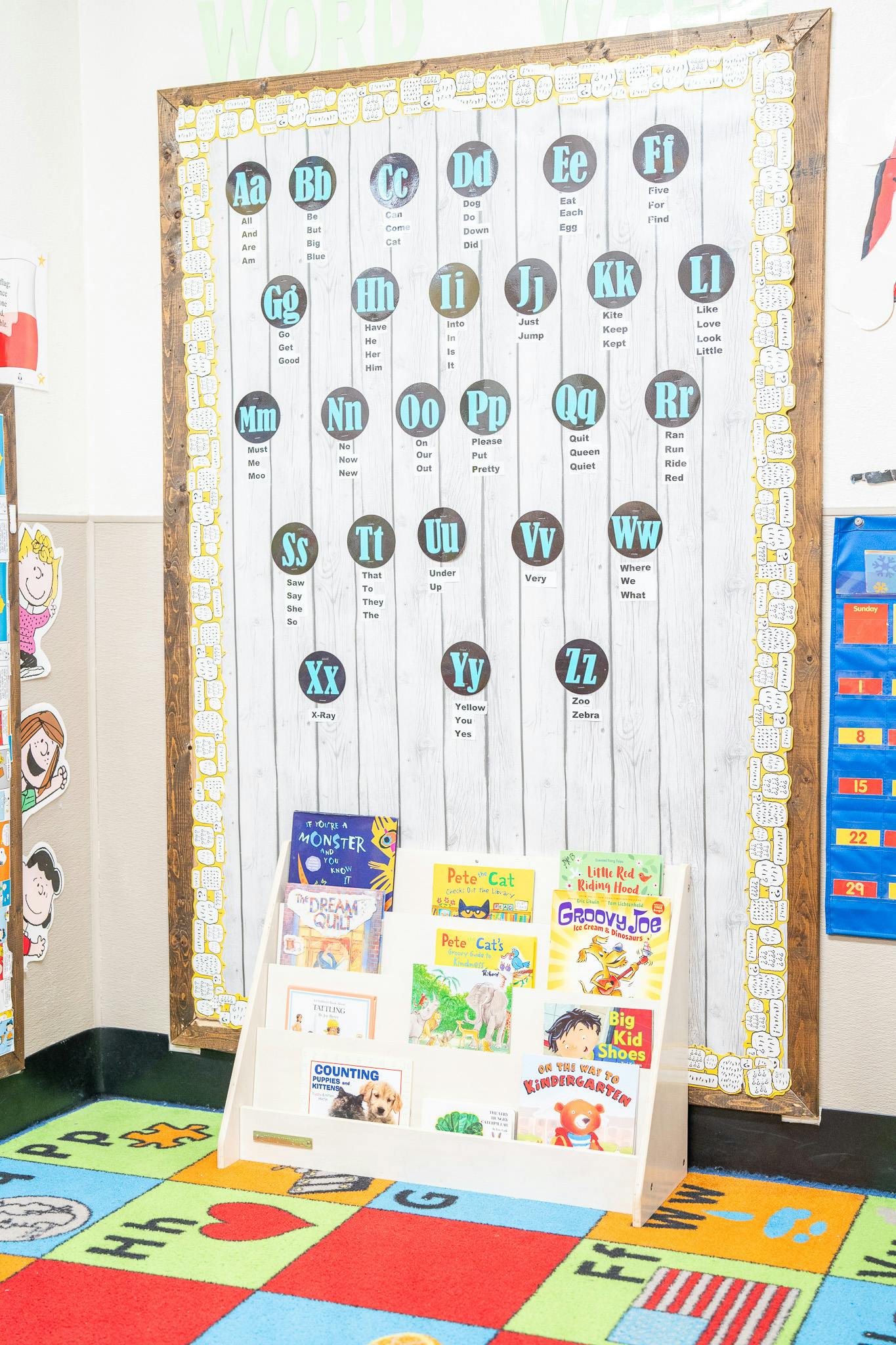 Classroom bookshelf displaying children picture books in front of an alphabet sign