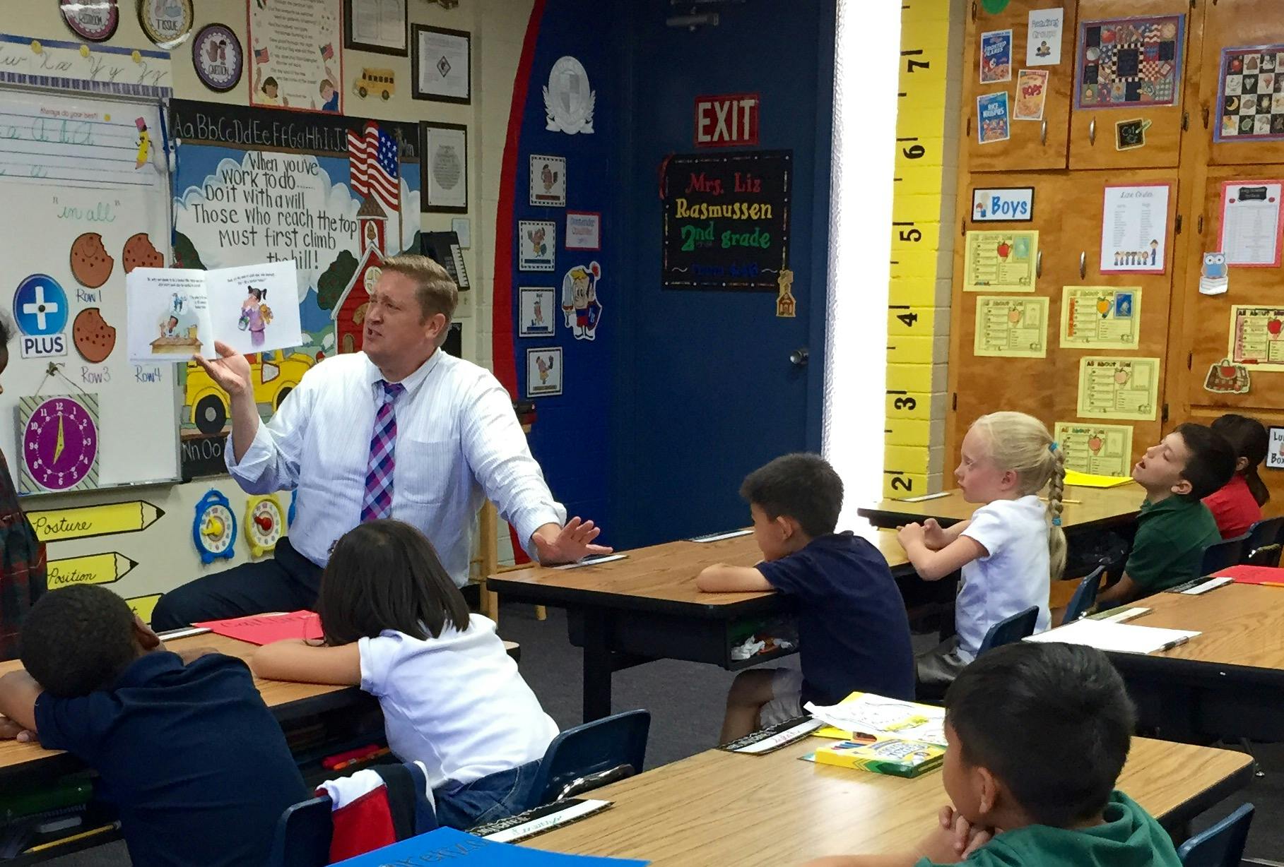 Adult holding a book and speaking to children in a classroom