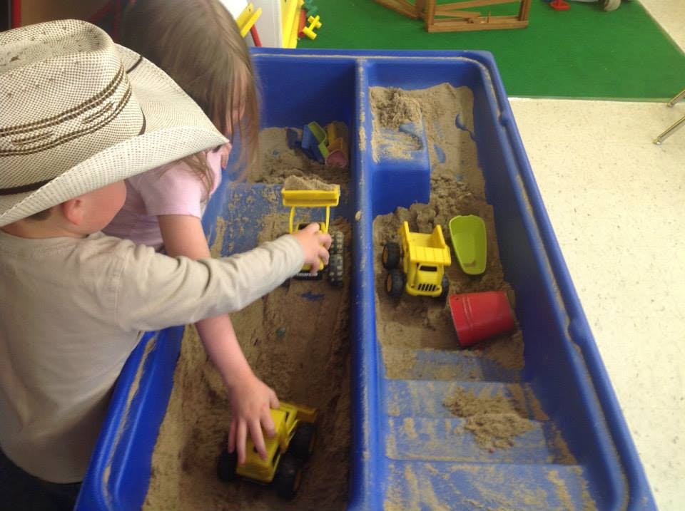 Child in a cowboy hat playing with toy trucks in a sand table