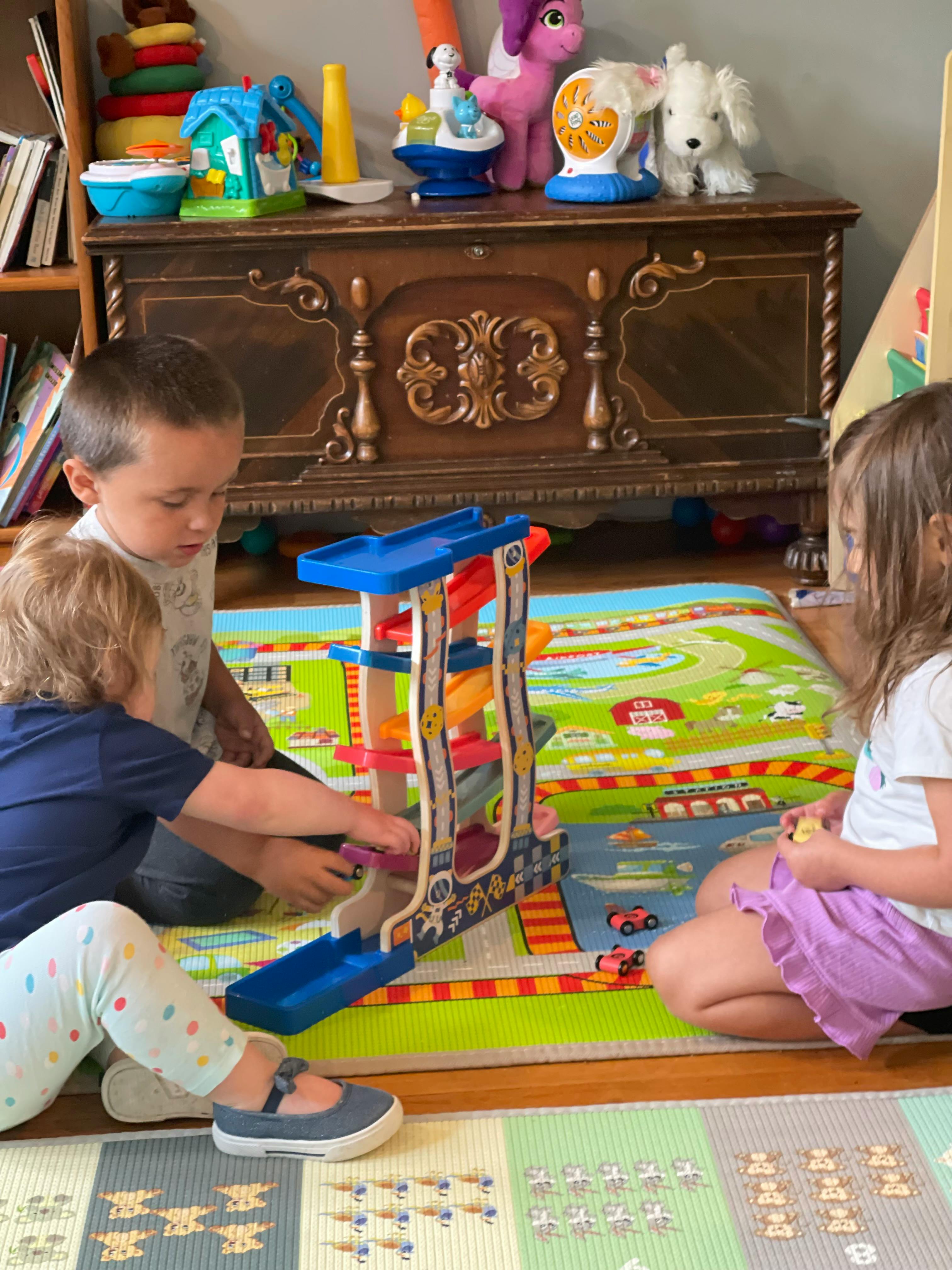 Three children playing with a toy car ramp on a mat