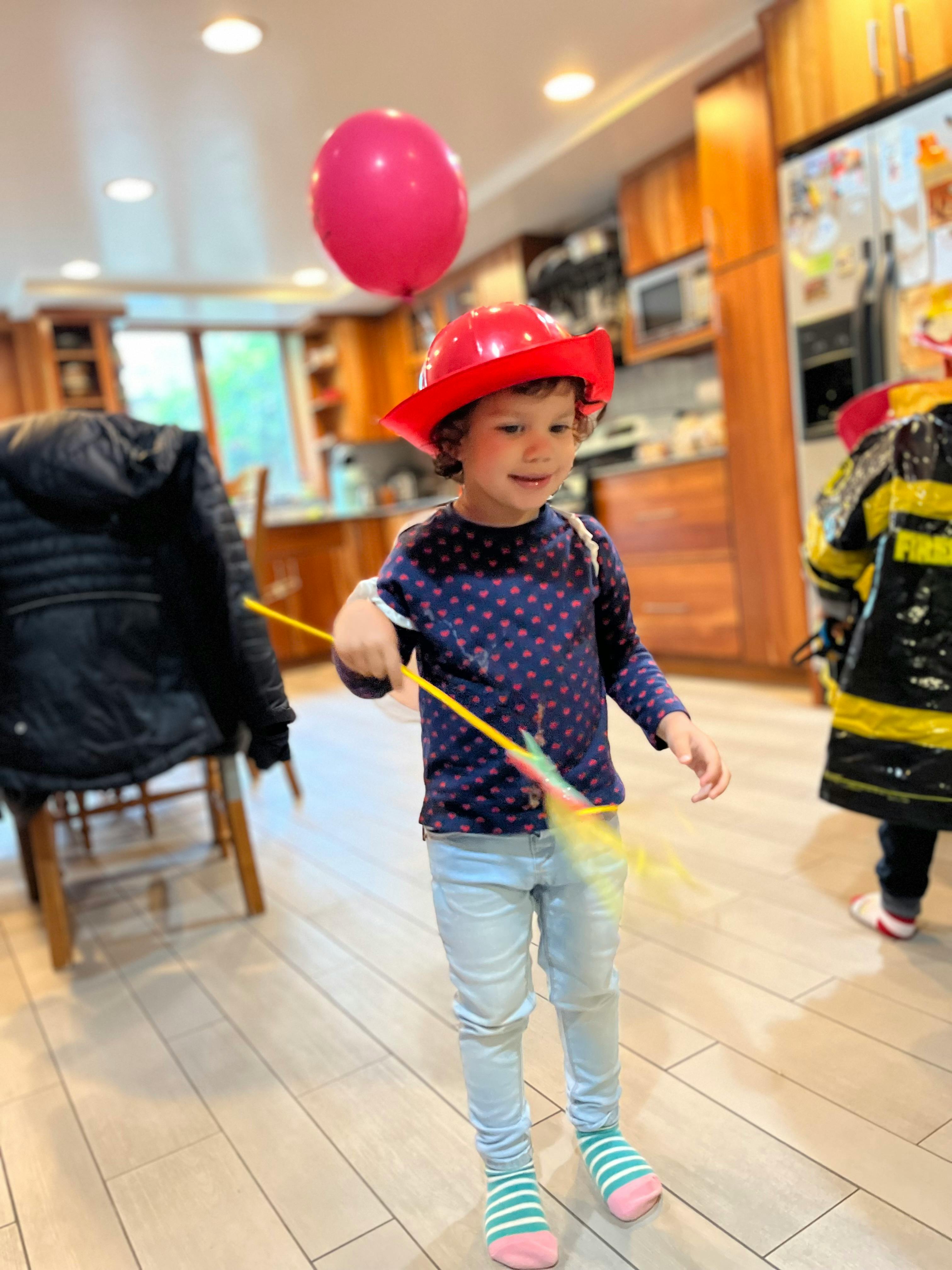 Child in a red hat holding a toy with a pink balloon floating nearby