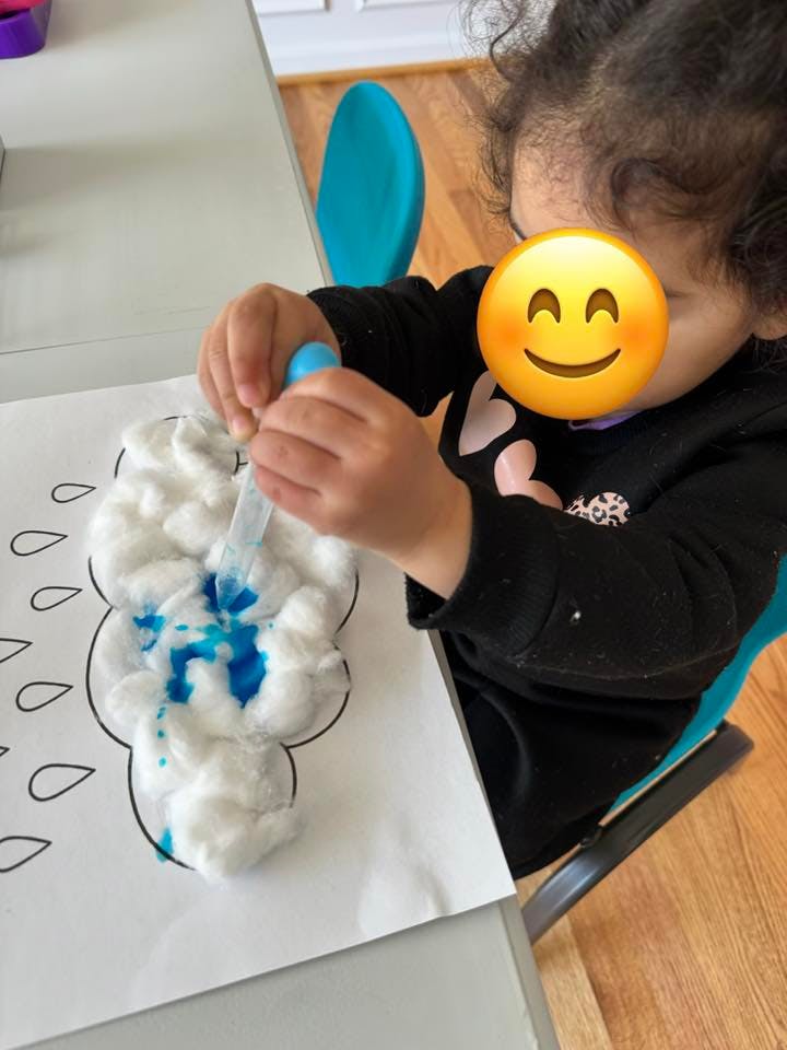 Child using a dropper to add blue liquid to cotton balls on a cloud drawing