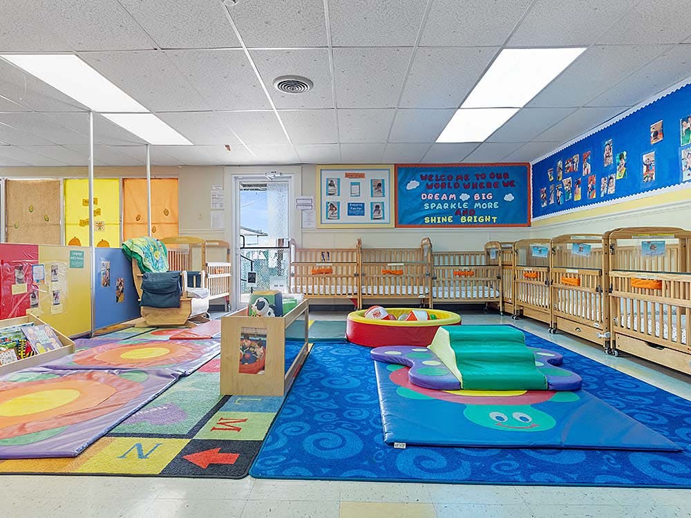 Baby room with multiple cribs, colorful mats, and play equipment