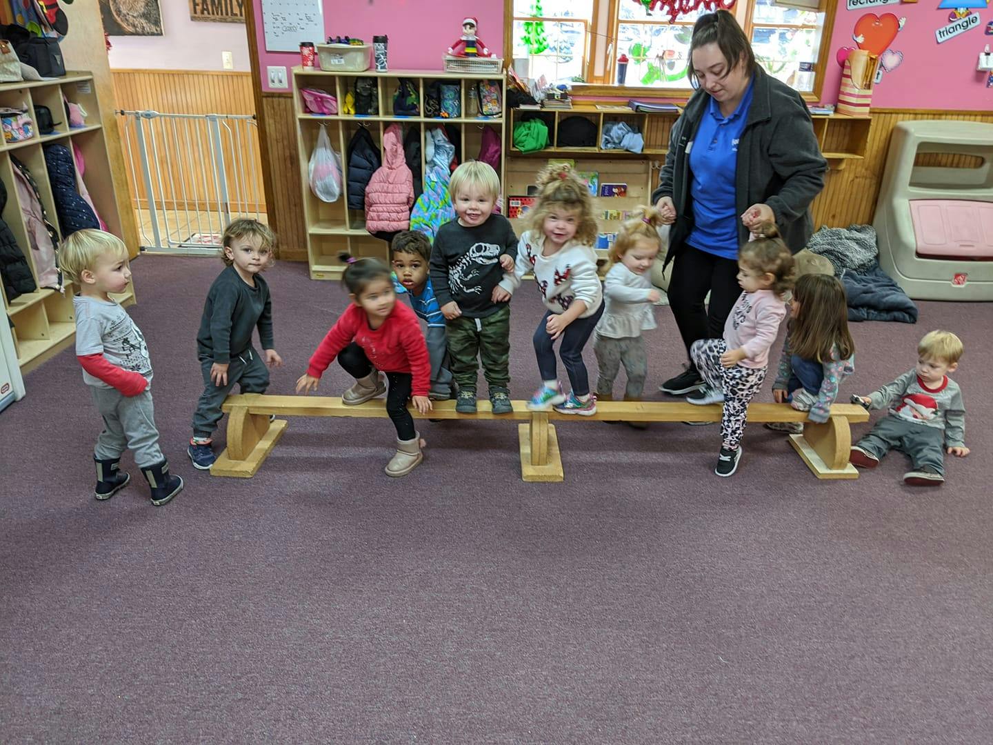 Adult supervising children playing on a low balance beam in a classroom