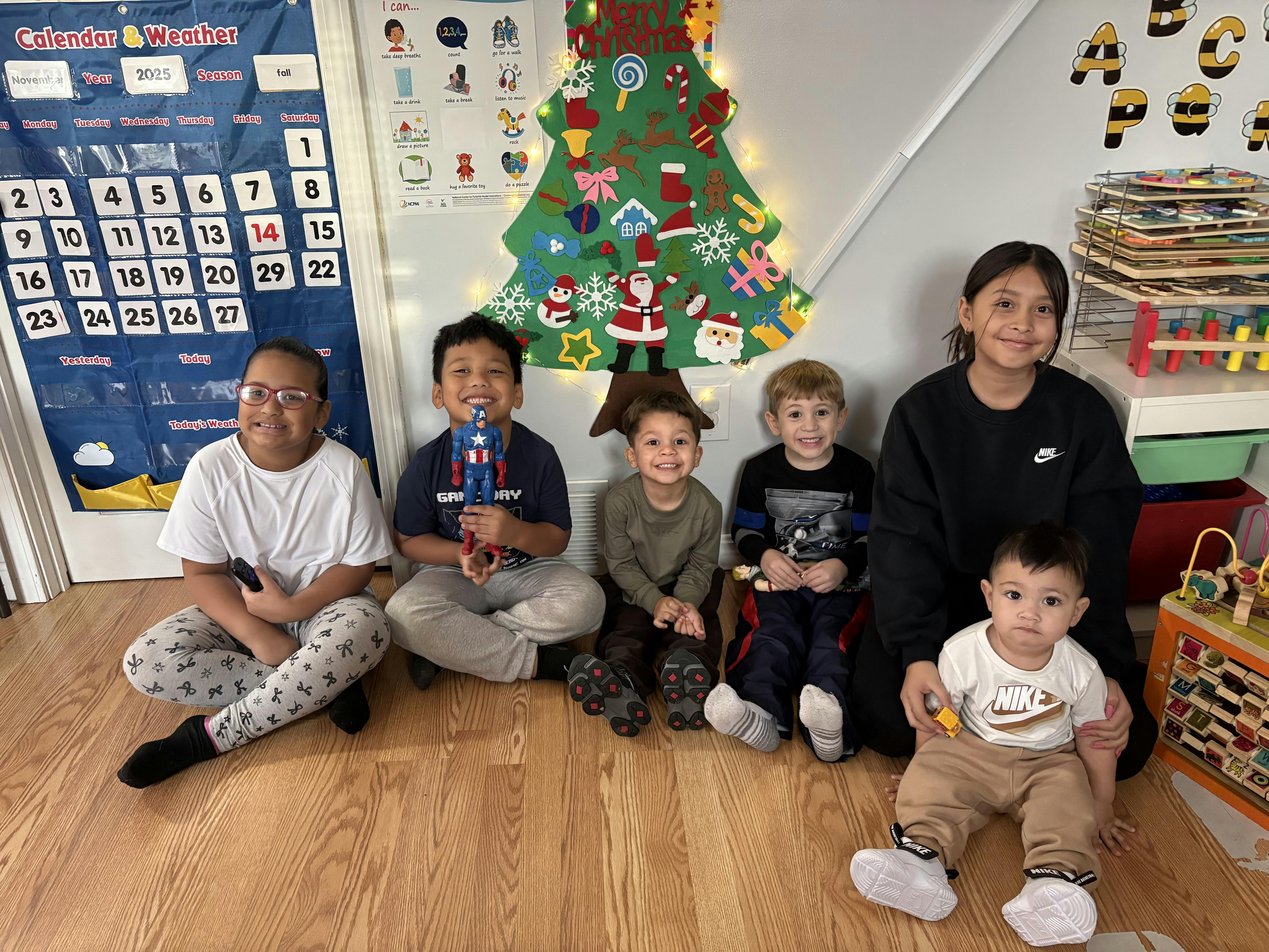 Group of children and an adult sitting on a wooden floor