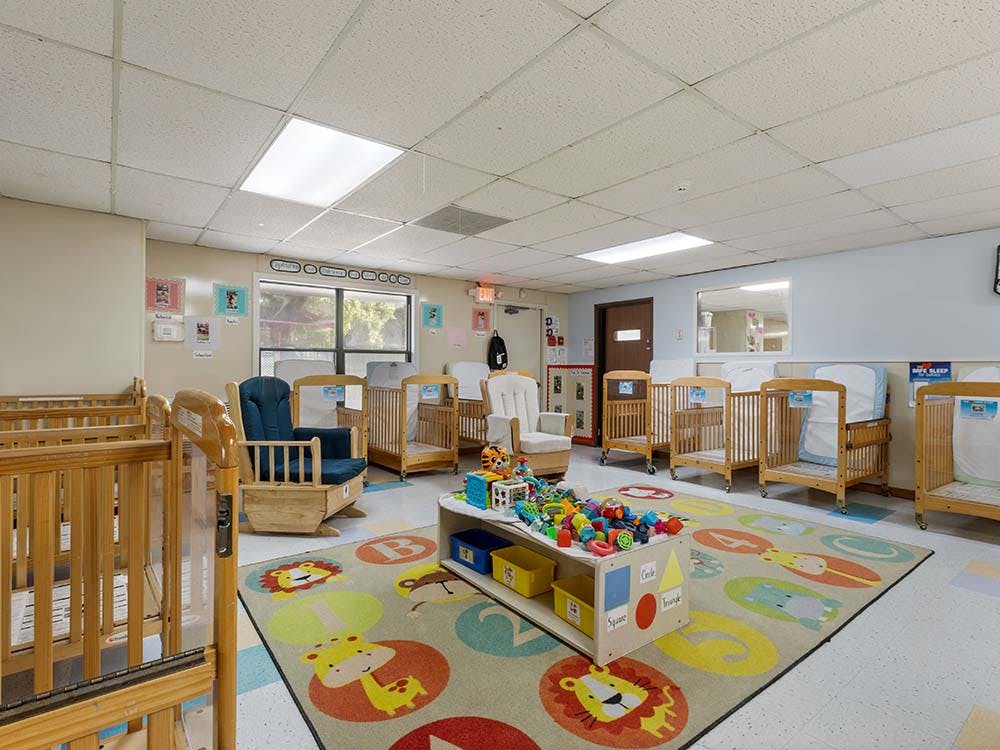 A room with multiple wooden cribs, a colorful rug, and a central toy shelf