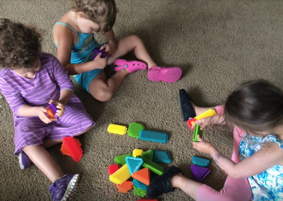 Three children playing with colorful building blocks on a carpet