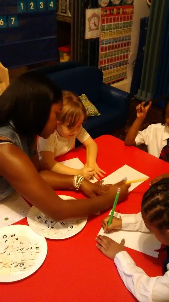 Adult and children at a red table, one child writing