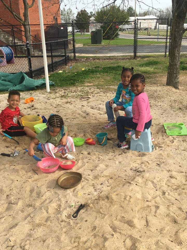 Three children playing in a sandbox with toys