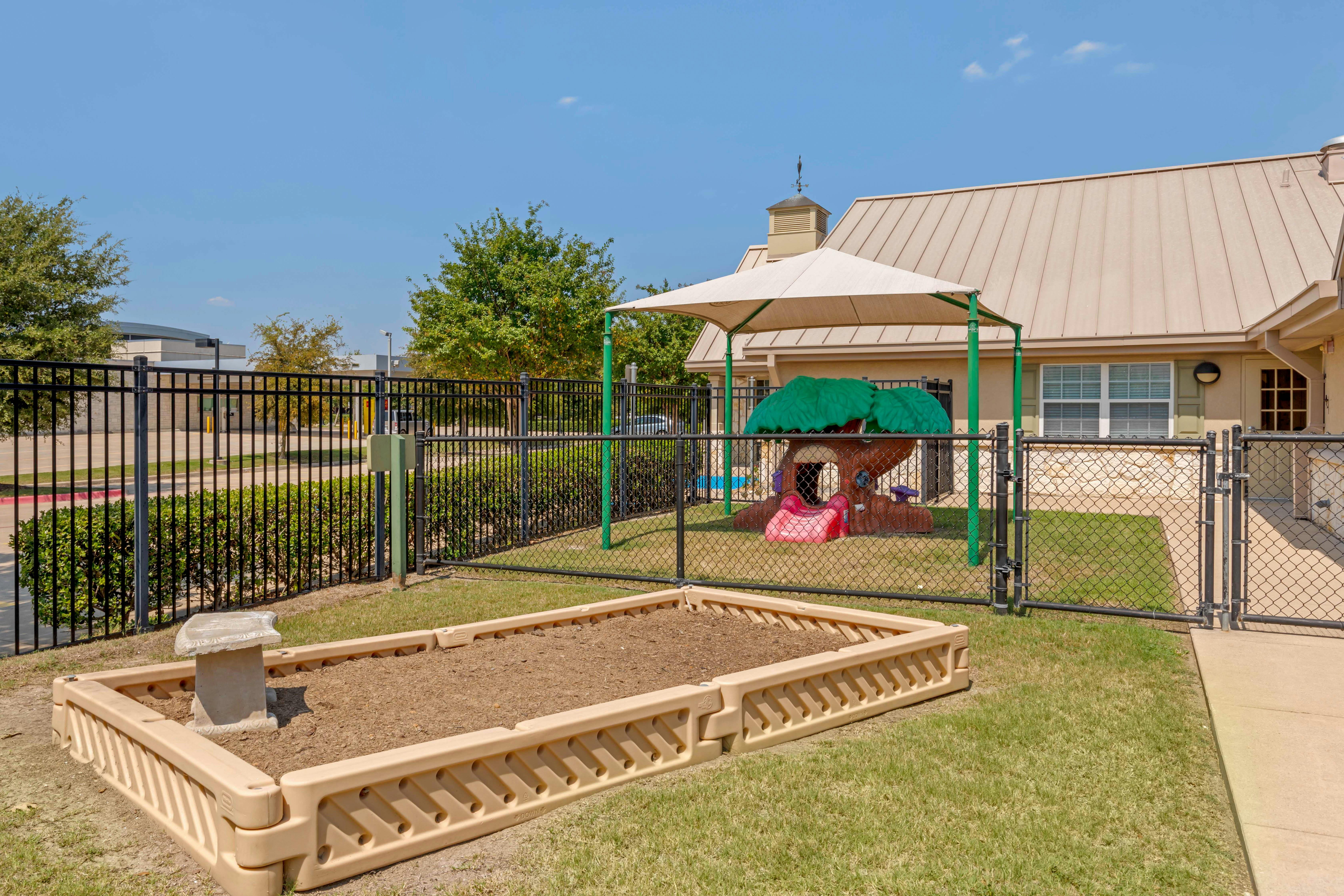 A fenced outdoor play area with a tree-shaped play structure and sandbox