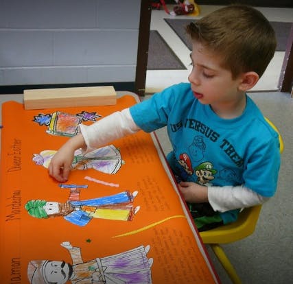 Child coloring a drawing on an orange mat at a table