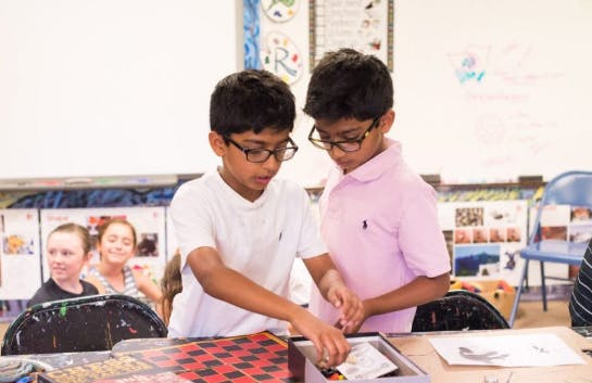 Two children in glasses looking at items in a box on a table