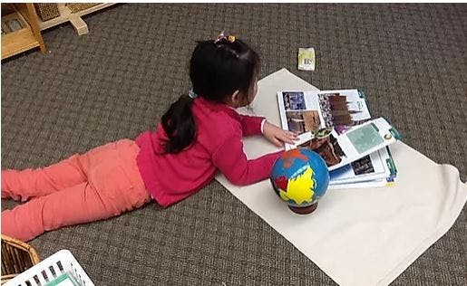 Child lying on floor looking at a book and globe