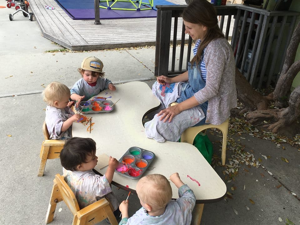 Adult and multiple children painting at a small table outdoors